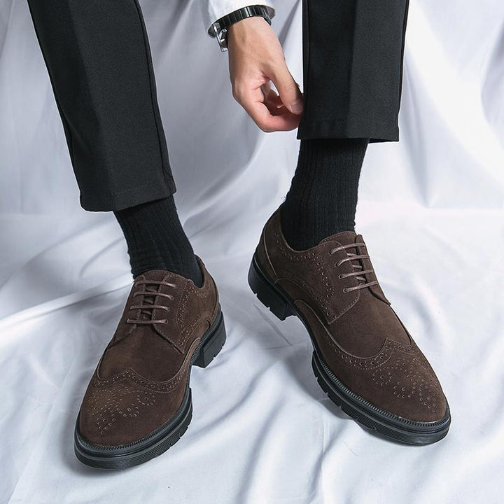 Man wearing dark brown suede brogue shoes with black socks and black trousers on white fabric background