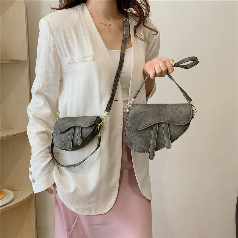 Woman wearing white blazer and pink skirt holding two gray leather crossbody bags with gold hardware
