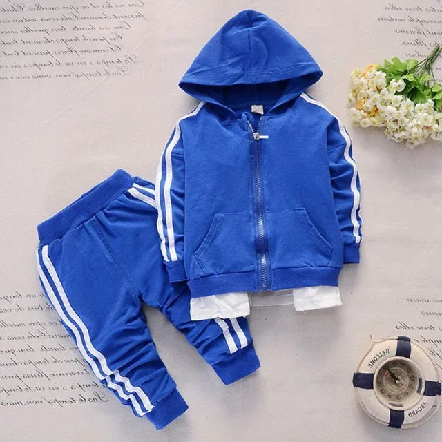 Blue toddler tracksuit with white stripes on sleeves and pant legs, displayed with white flowers and nautical decor