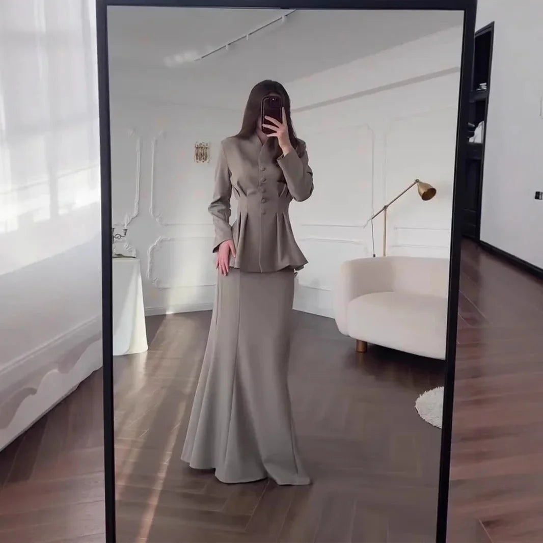 Woman in beige fitted blazer and long skirt taking mirror selfie in stylish modern room