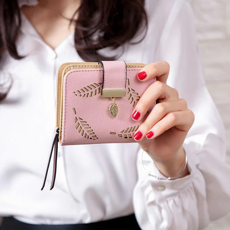 Woman holding pink leather wallet with leaf cutout design and gold leaf charm, wearing white blouse