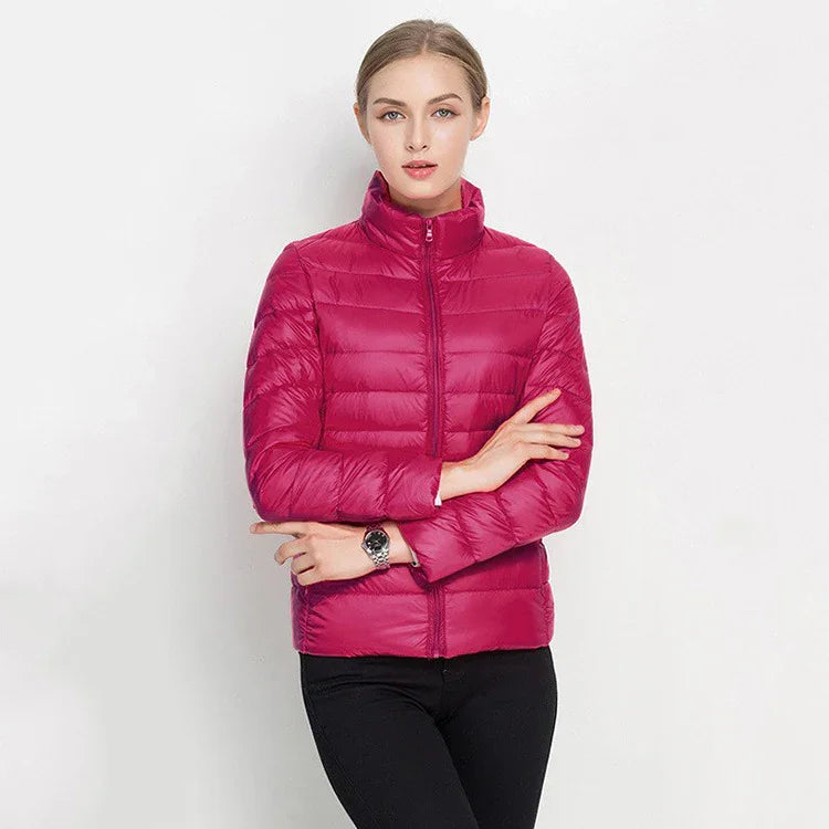 Woman wearing a bright pink quilted puffer jacket with a high collar and black pants against a white background
