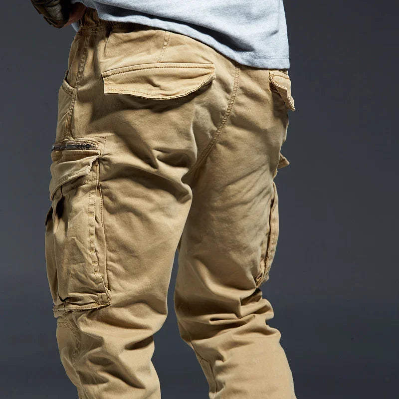 Close-up of beige cargo pants with multiple pockets and zipper detail on grey background