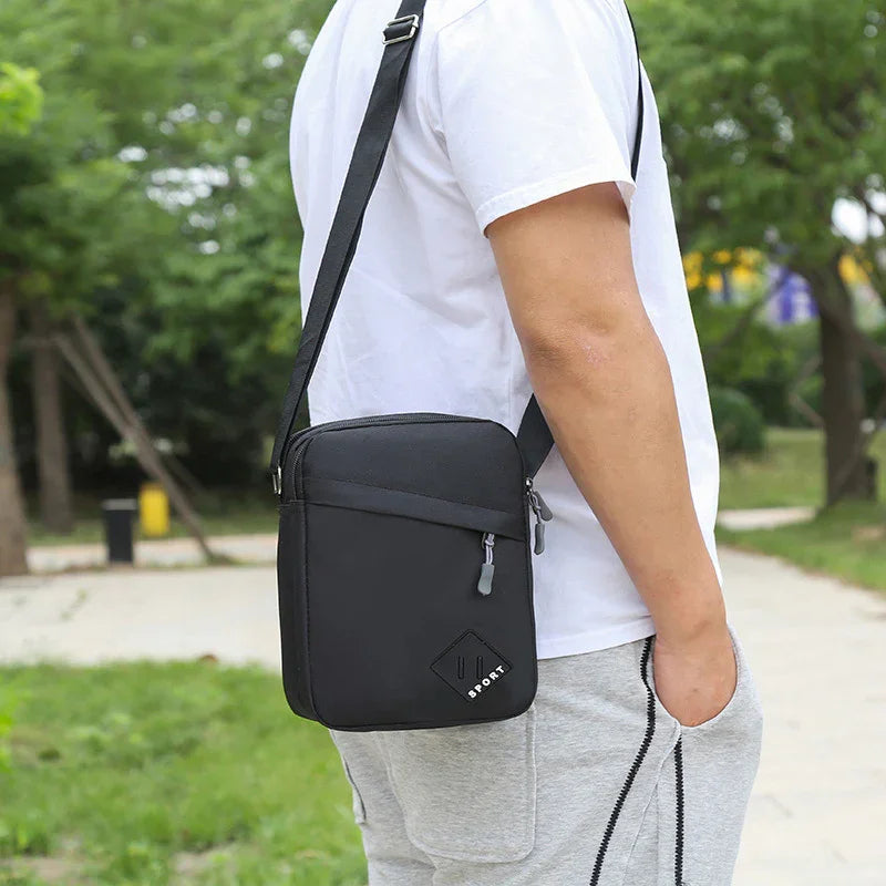 Black sport crossbody bag worn by person in white t-shirt and gray pants outdoors