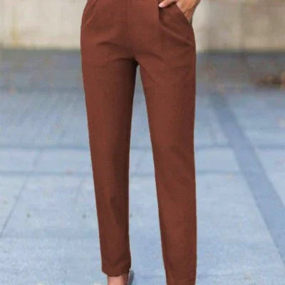Woman wearing slim-fit rust brown pants standing outdoors on a paved surface