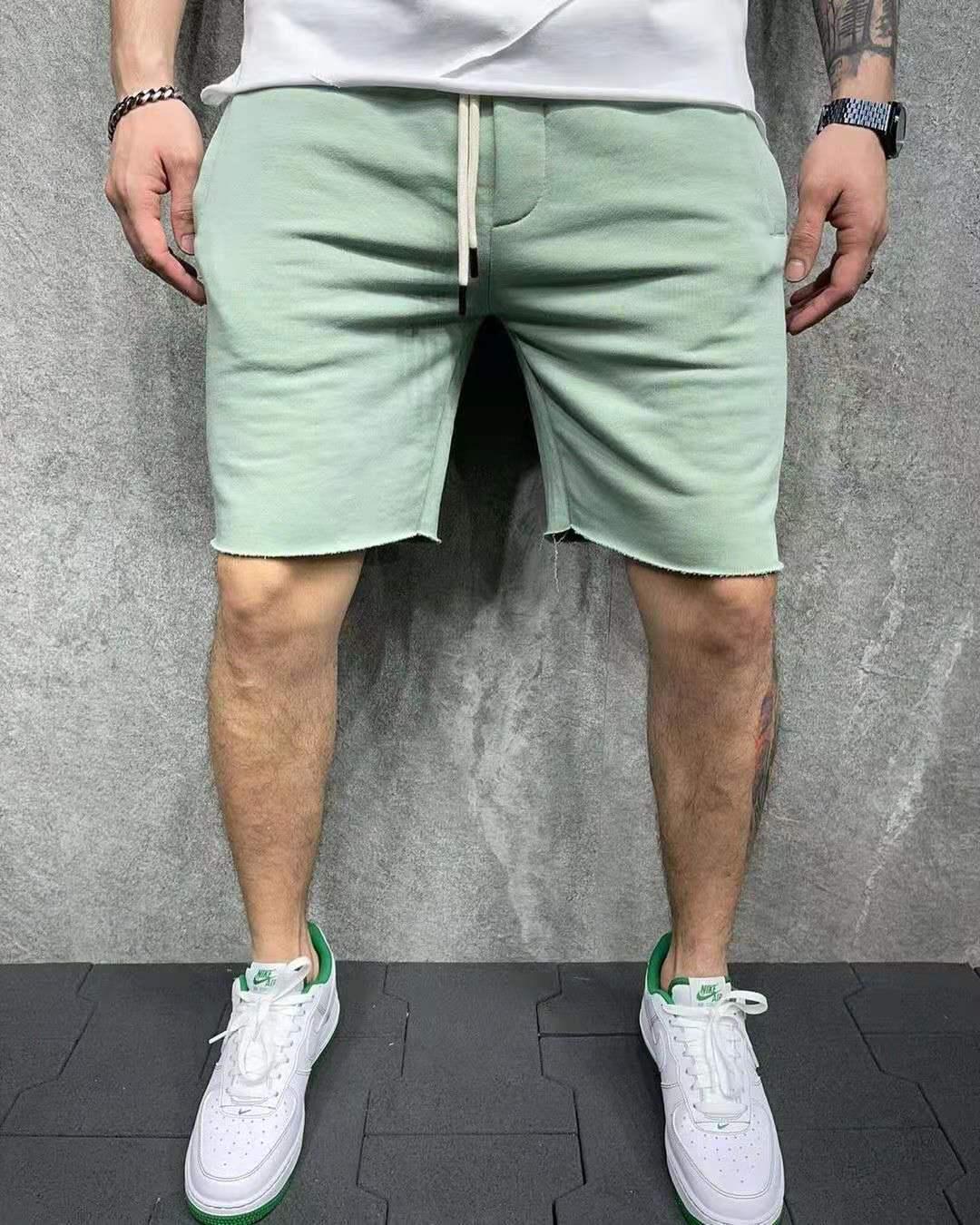 Man wearing light green casual shorts with raw hem and white Nike sneakers with green accents