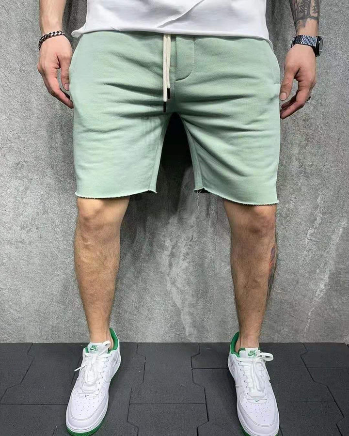 Man wearing light green casual shorts with raw hem and white Nike sneakers with green accents