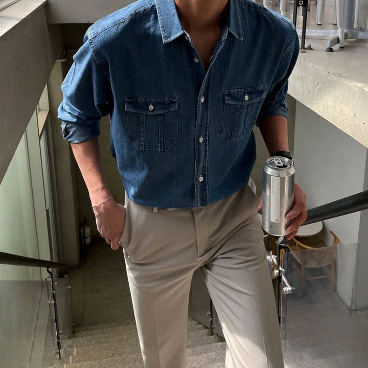 Man wearing blue denim shirt and beige pants walking upstairs holding a silver can