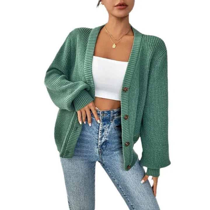 Woman wearing oversized green knit cardigan with buttons, white crop top, and high-waisted blue jeans