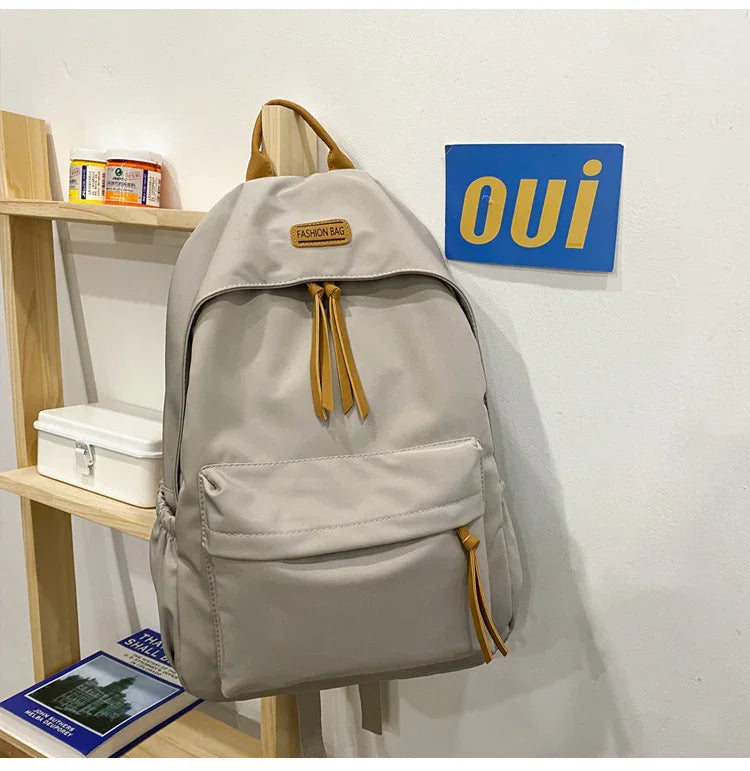 Beige fashion backpack with brown zipper pulls hanging on wooden shelf next to blue and yellow 'oui' wall sign