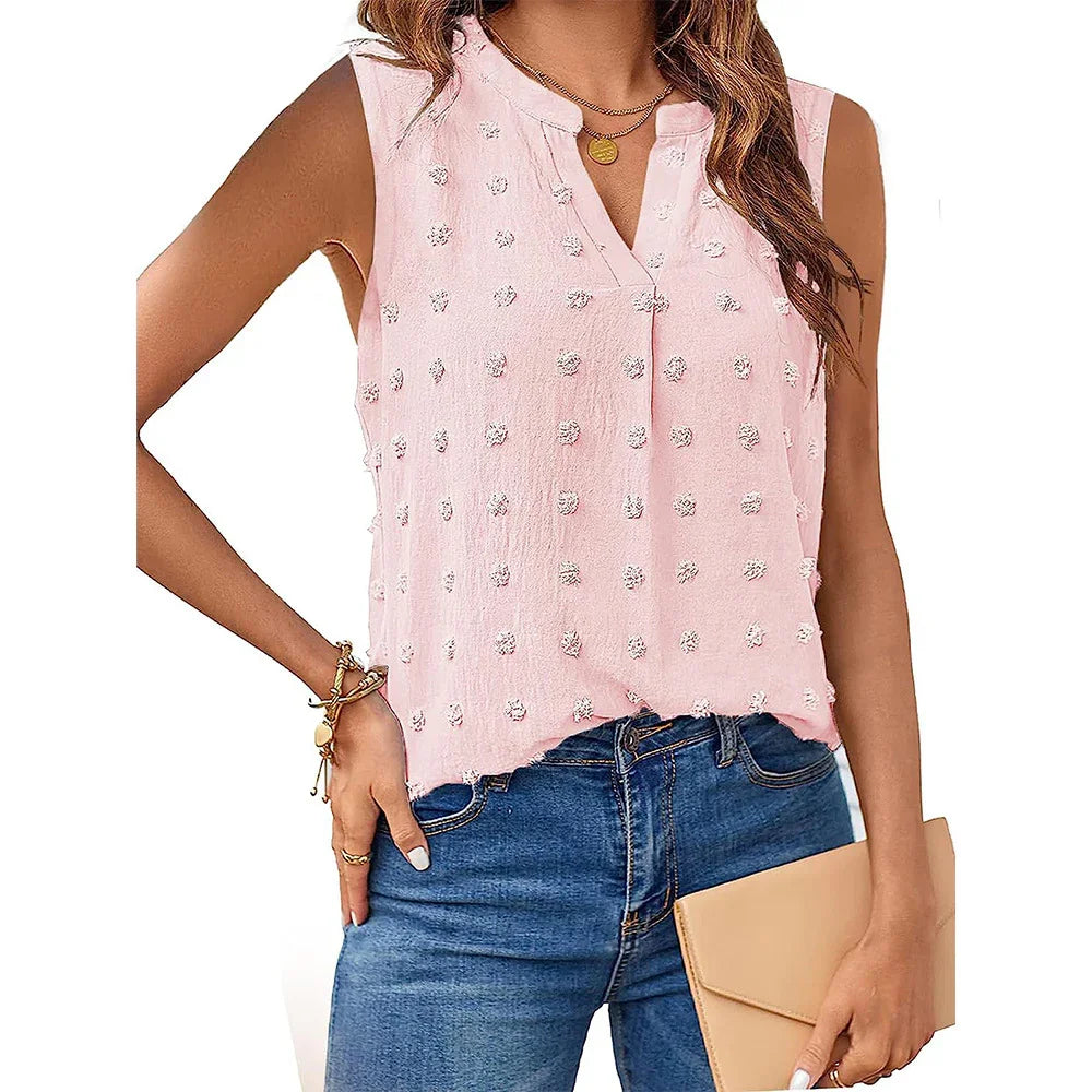 Woman wearing pink sleeveless textured blouse with polka dot details and blue jeans holding beige clutch