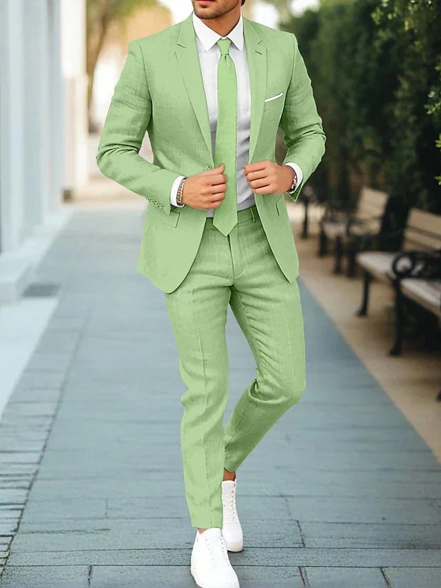 Man wearing a light green slim-fit suit with matching tie, white shirt, and white sneakers walking on a sidewalk