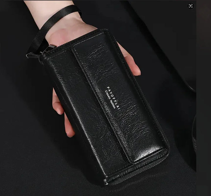 Hand holding black leather wristlet wallet with PAYOFFLAN Classic Fashion logo on dark background