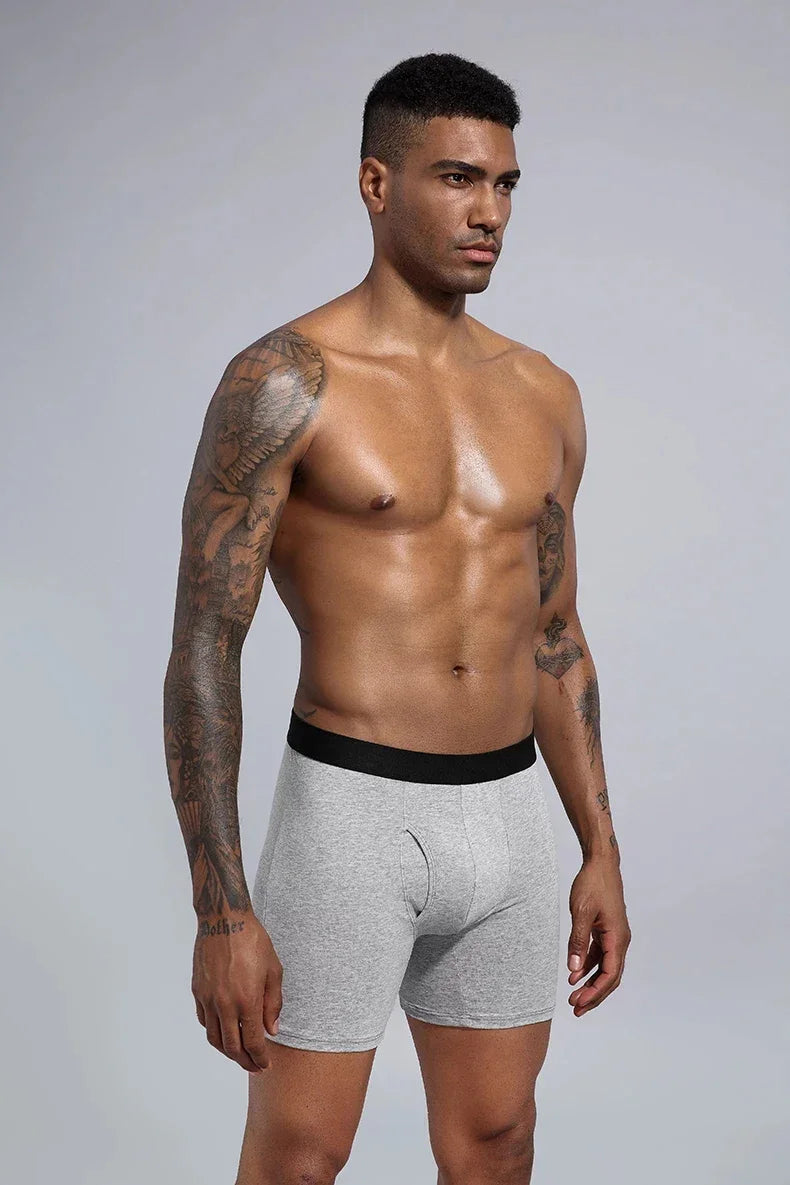 Muscular man with sleeve tattoos wearing grey boxer briefs with black waistband on neutral background