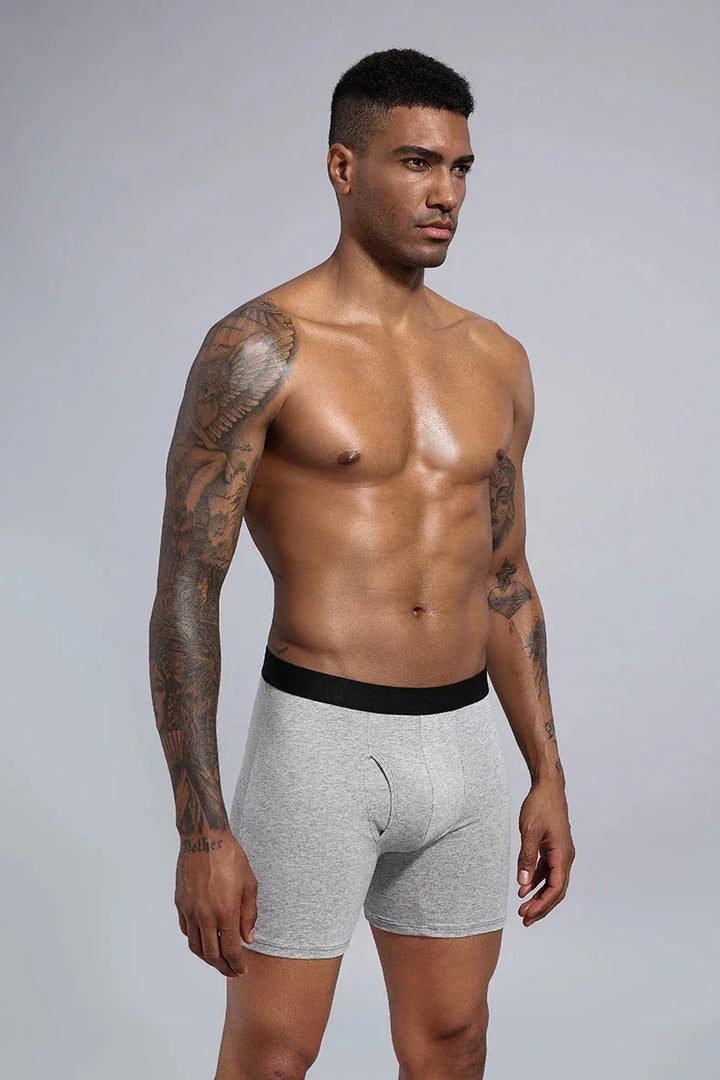 Muscular man with sleeve tattoos wearing grey boxer briefs with black waistband on neutral background