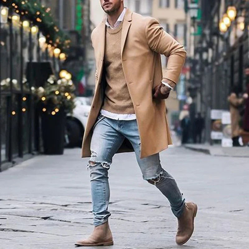 Man wearing camel overcoat, tan sweater, ripped light blue jeans, and brown boots walking on city street