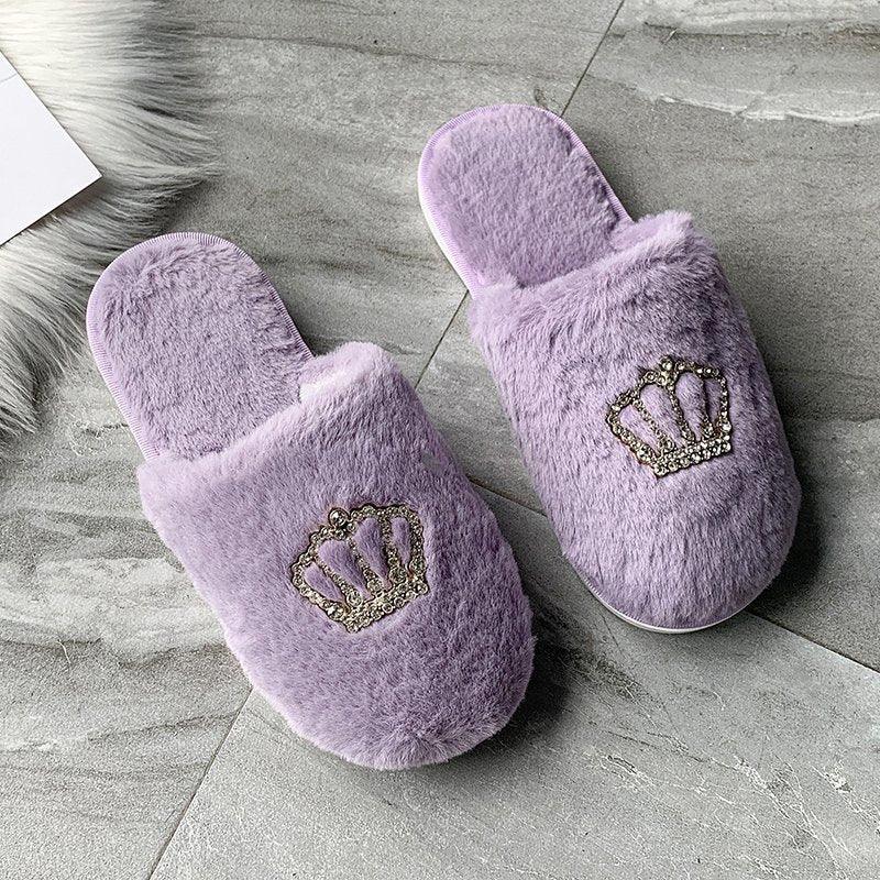 Pair of cozy lavender faux fur slippers with jeweled crown embellishments on a gray marble floor