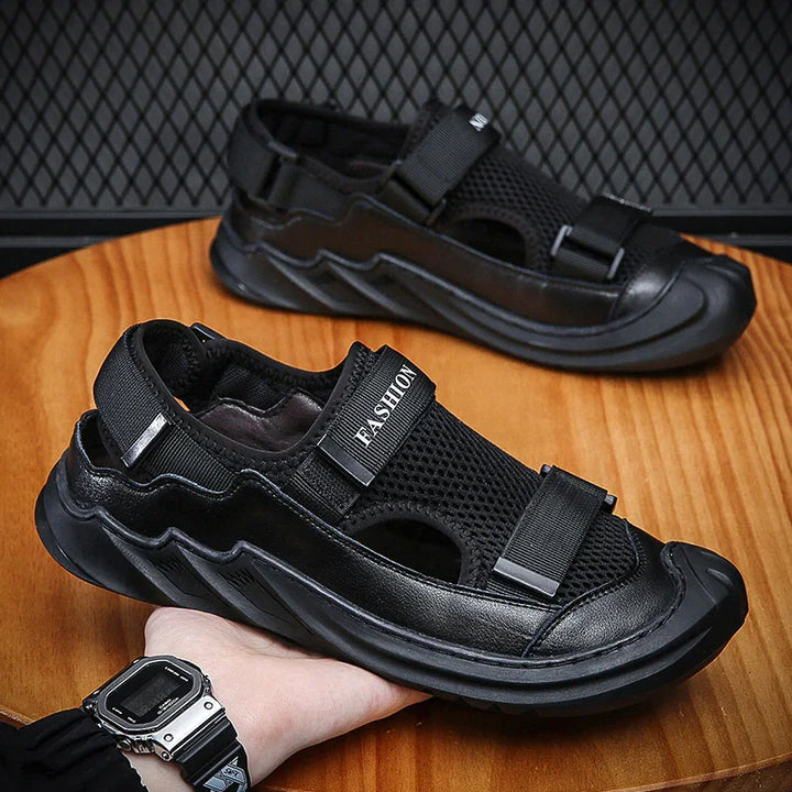 Black mesh and leather men's sandals with velcro straps on a wooden surface