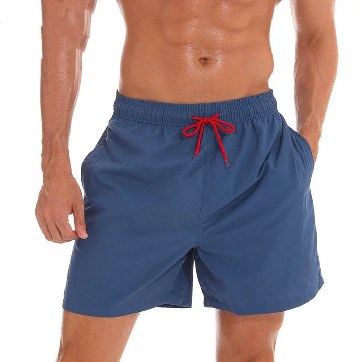 Men's blue swim shorts with red drawstring worn by shirtless muscular model