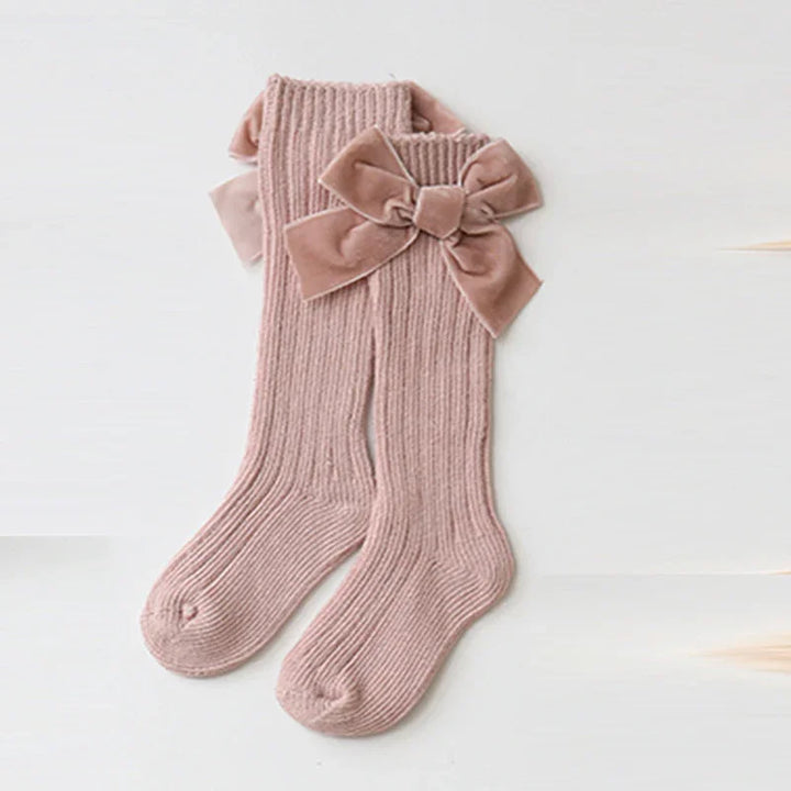 Pink ribbed knit baby socks with large velvet bows on white background