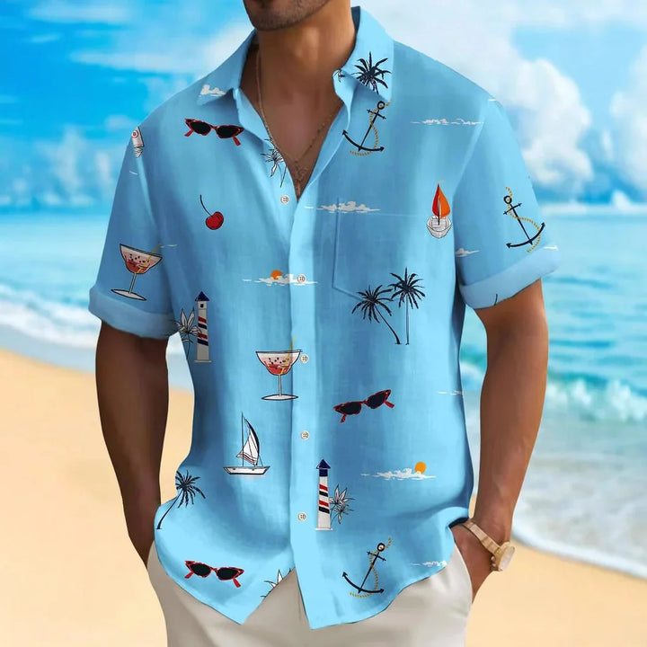 Man wearing blue short-sleeve beach shirt with sailboats, anchors, palm trees, and cocktail prints