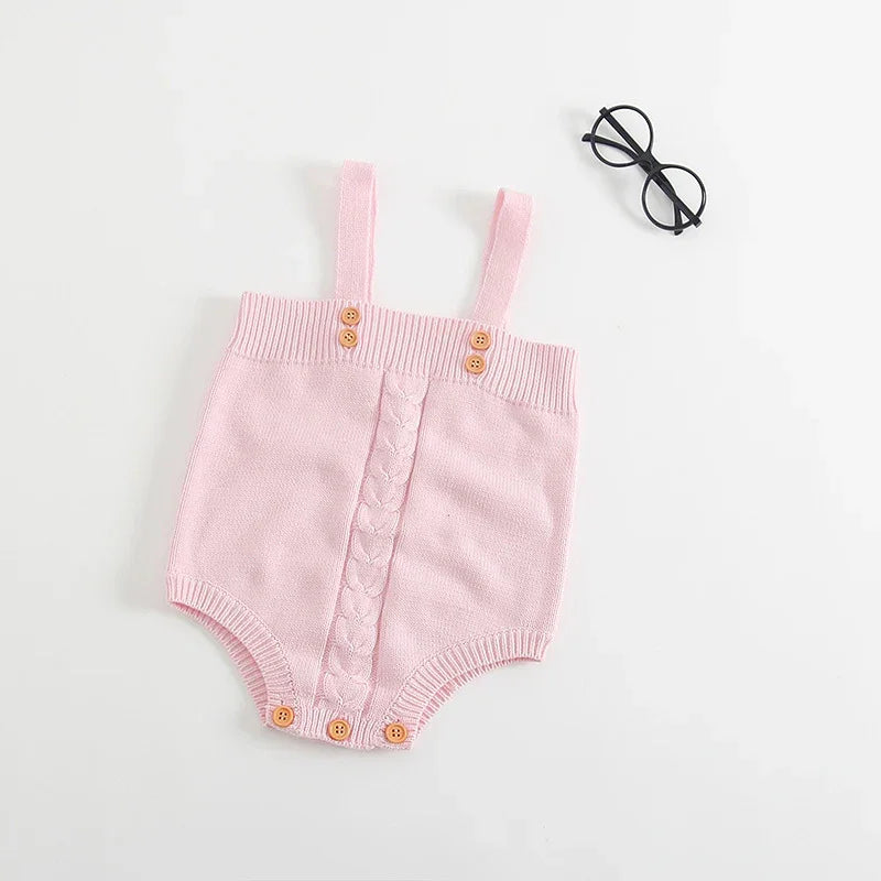 Pink knitted baby romper with buttons and straps beside black round glasses on white background