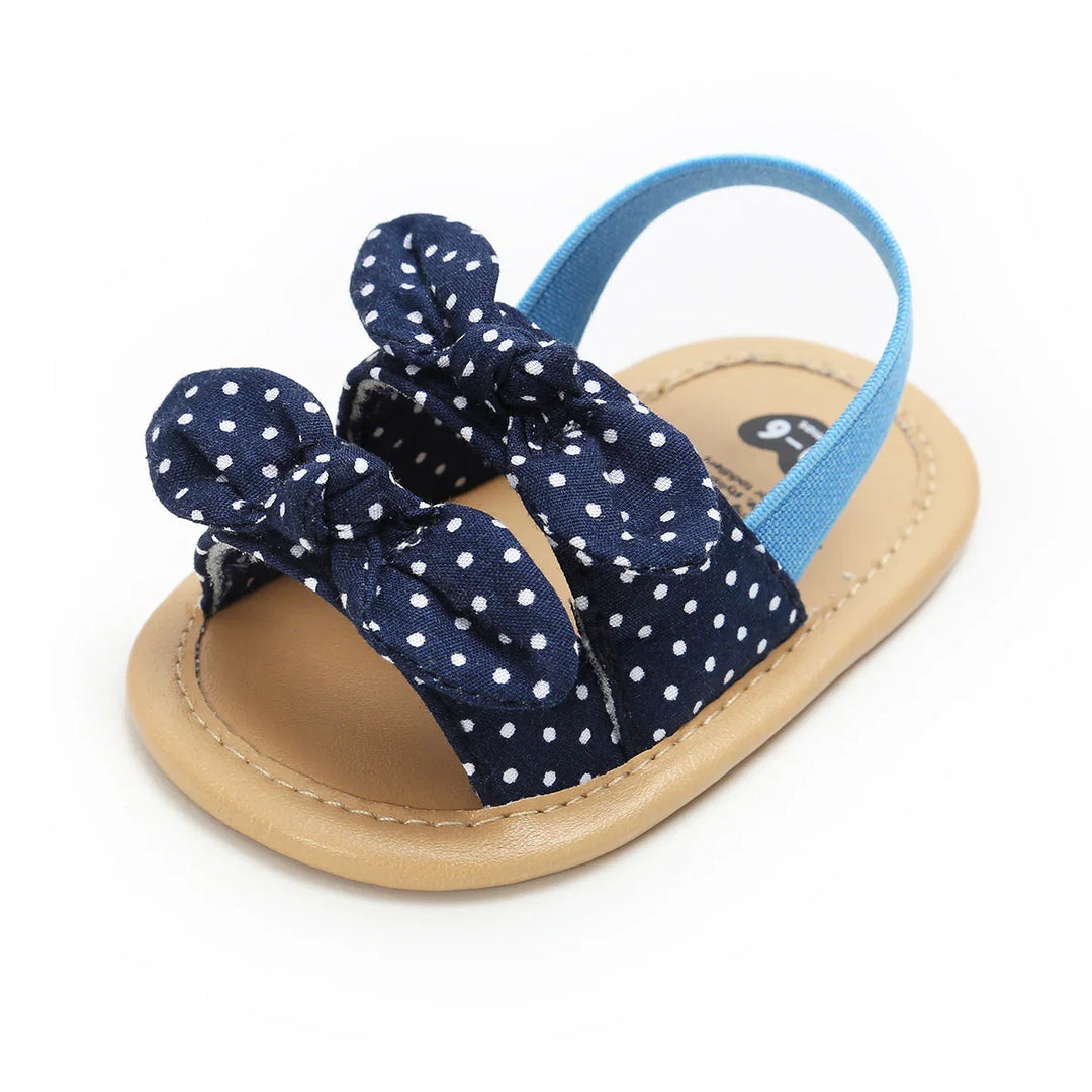 Baby sandal with tan sole and navy blue polka dot fabric straps with bows and blue ankle strap