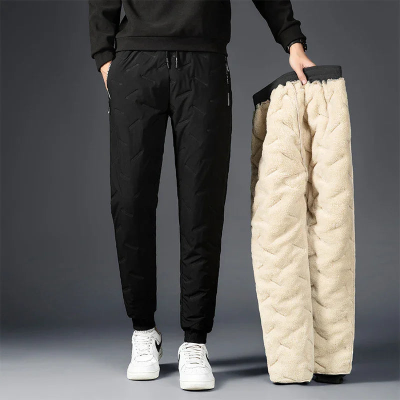 Man wearing black quilted jogger pants holding fleece-lined pants against gray background
