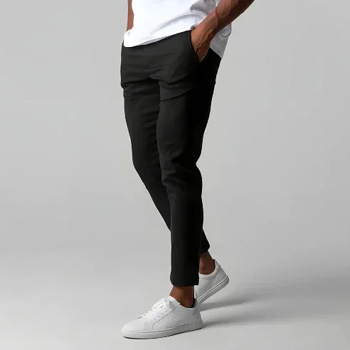 Man wearing black slim-fit pants with white sneakers and white shirt on gray background