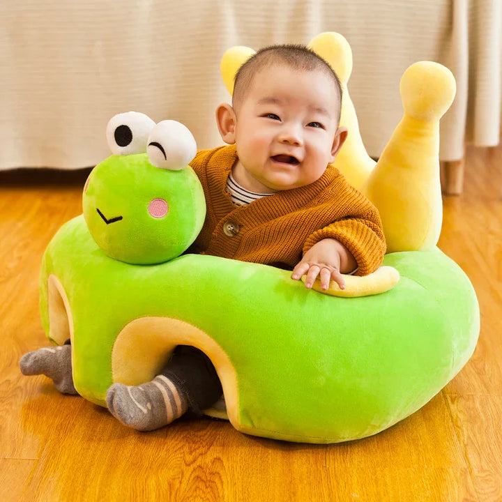 Smiling baby sitting in a green plush snail seat on wooden floor with beige curtains