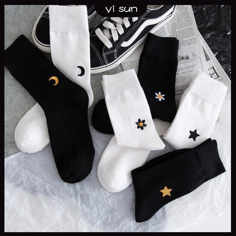 Black and white socks with embroidered stars, moons, and flowers, styled with black sneakers on a modern backdrop