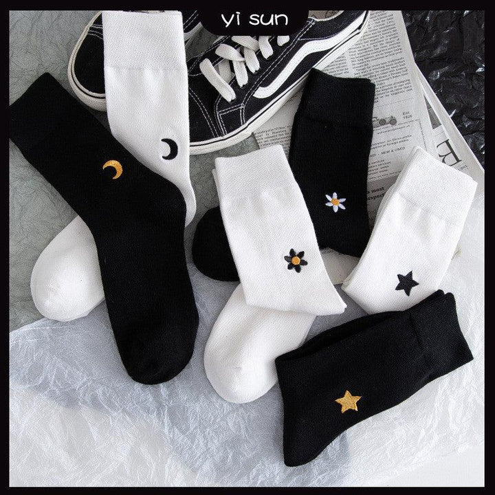 Black and white socks with embroidered stars, moons, and flowers, styled with black sneakers on a modern backdrop