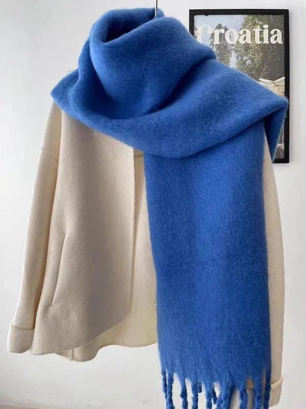 Beige coat hanging with a thick, soft blue scarf draped over it against a white wall with Croatia framed print