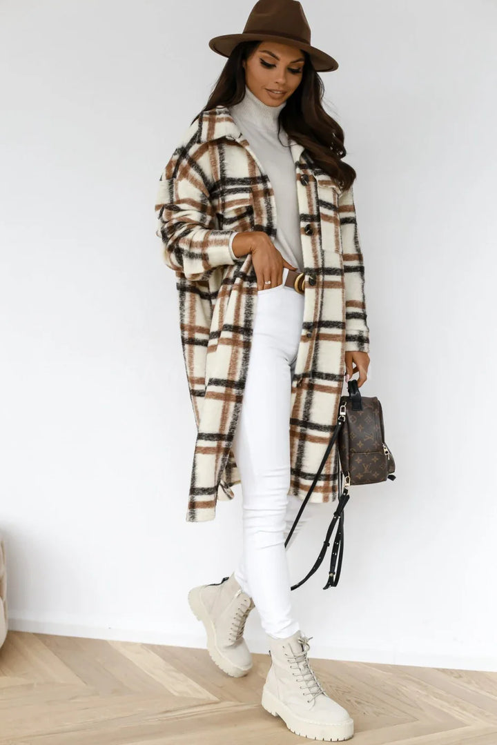 Woman in brown hat, plaid long coat, white turtleneck, white pants, and beige lace-up boots holding a designer backpack