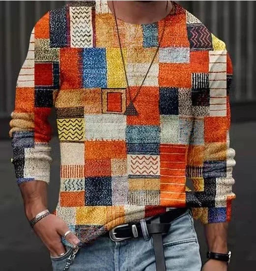 Men's colorful patchwork sweater with geometric shapes in orange, blue, yellow, and black paired with light denim jeans
