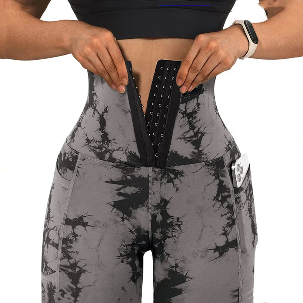 Woman wearing black and gray tie-dye workout leggings with side pocket holding phone and waist trainer