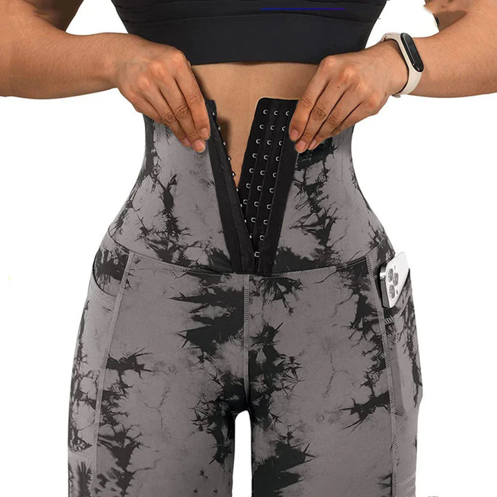 Woman wearing black and gray tie-dye workout leggings with side pocket holding phone and waist trainer