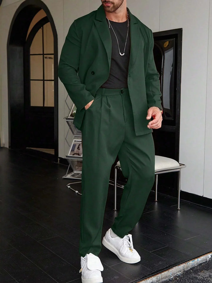 Man wearing dark green suit with black shirt and white sneakers indoors