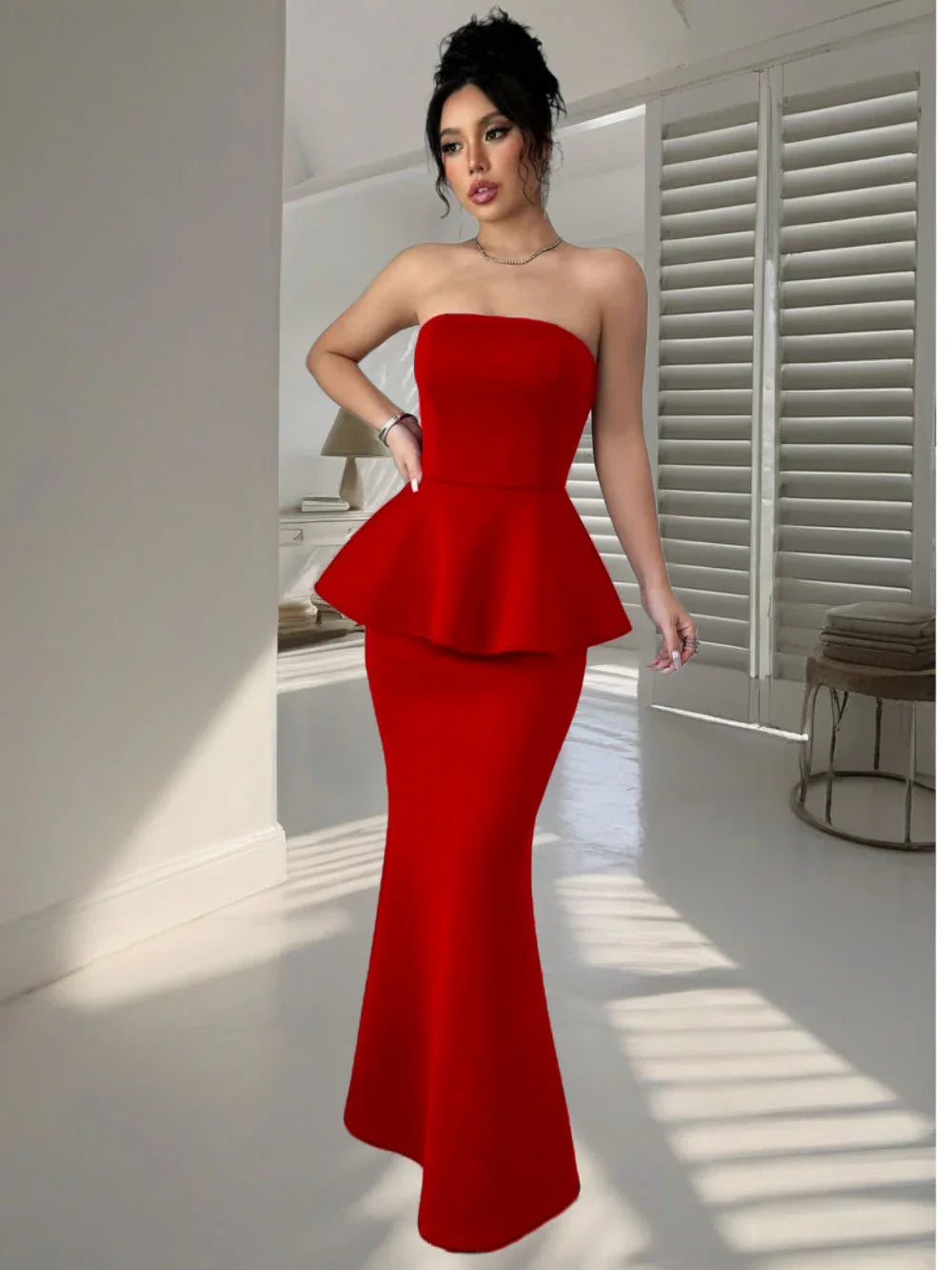 Woman in elegant red strapless peplum evening gown standing indoors with light and shadows