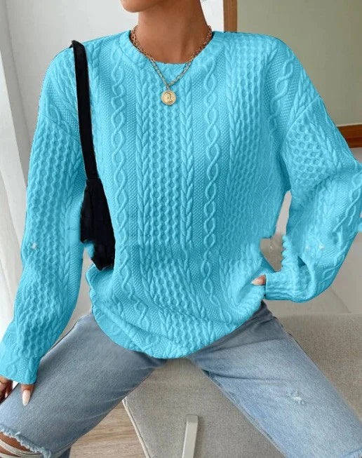Woman wearing sky blue cable knit sweater and ripped light blue jeans, accessorized with gold necklace and black shoulder bag