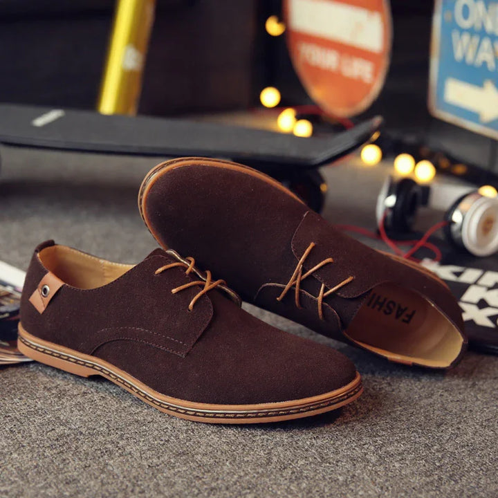 Brown suede casual lace-up shoes on carpet with skateboard and headphones in background