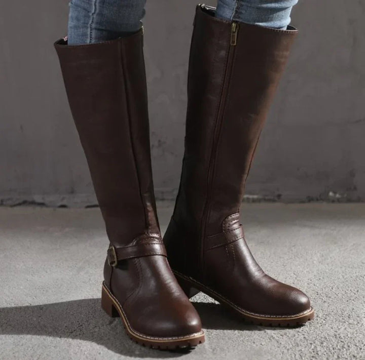 Brown knee-high leather boots with buckle detail and zipper, worn with blue jeans