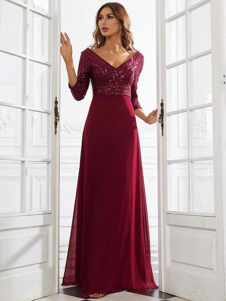 Woman in burgundy sequin top evening gown with 3/4 sleeves standing in white elegant room