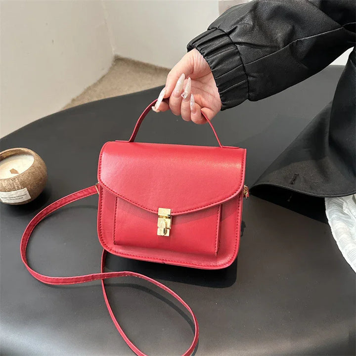 Red leather handbag with gold lock held on black table, styled with black sleeve and decorative candle