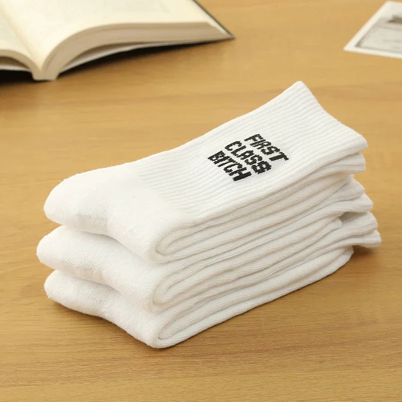 Stack of white ribbed socks on wooden table with text "FIRST CLASS BITCH"