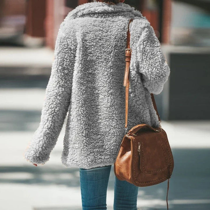 Woman wearing gray sherpa fleece jacket and carrying brown leather crossbody bag outdoors
