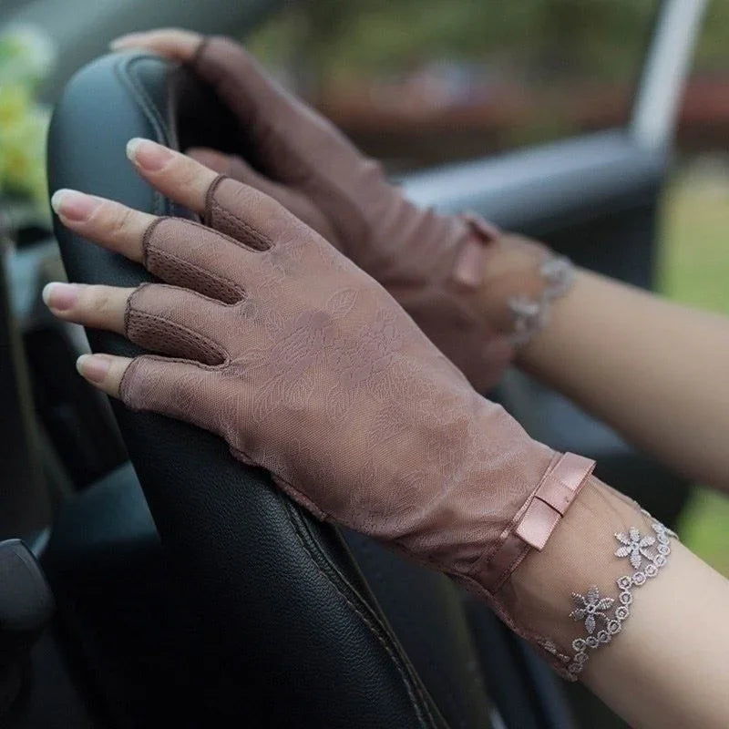 Hands wearing elegant brown lace fingerless gloves with bow and floral bracelet on car steering wheel