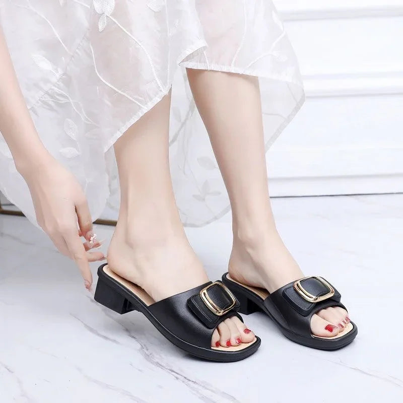 Women wearing black open-toe block heel sandals with gold buckle detail on marble floor