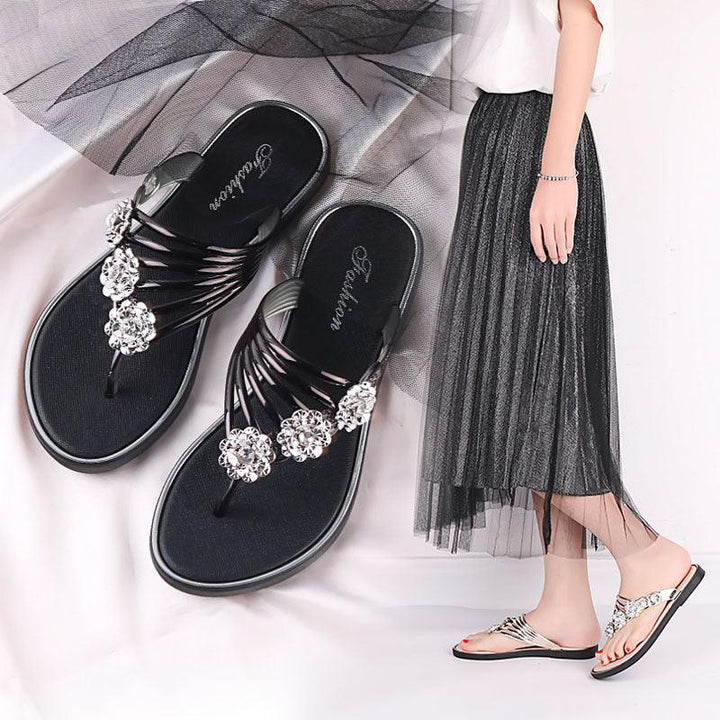 Black flat sandals with decorative rhinestone flowers worn with a black tulle skirt and white top
