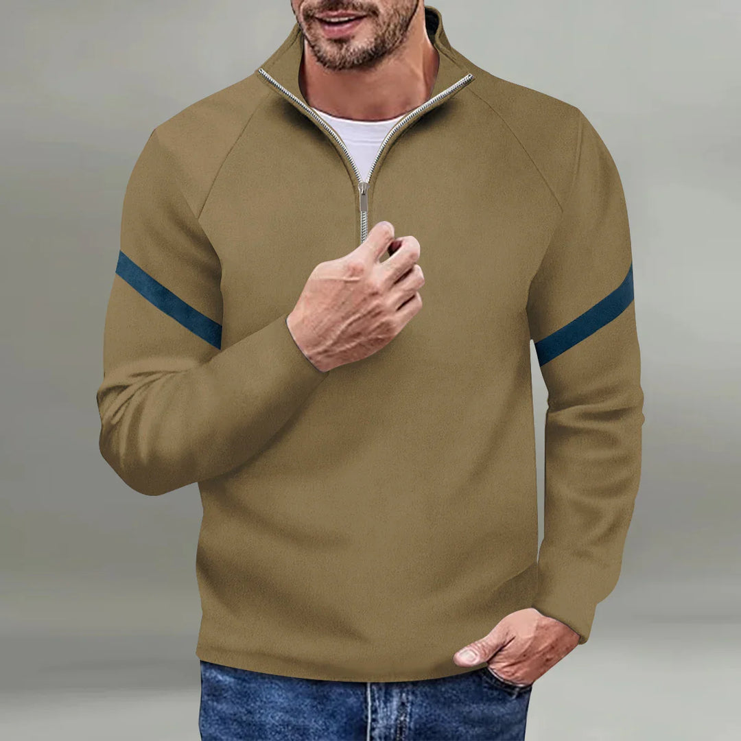 Man wearing olive green quarter-zip pullover with navy arm stripes and blue jeans